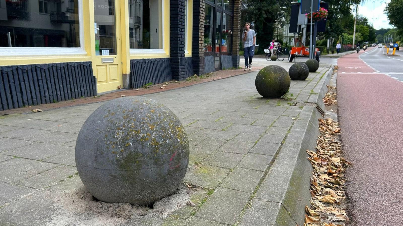 Rangée de boules en béton au bord d'un trottoir, le long d'une rue commerçante