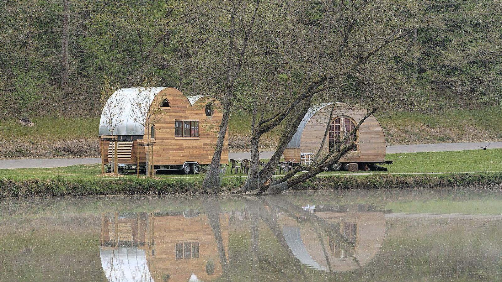 Deux tiny houses à bardage bois posées au bord d'un étang, entourées d'arbres