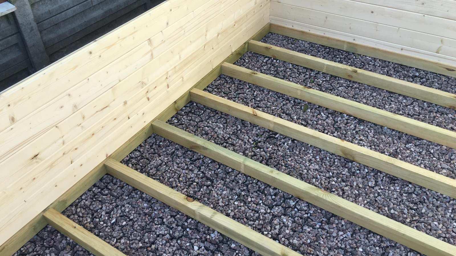Lambourdes en bois alignées sur une base remplie de gravier, au pied des parois d'un abri de jardin en cours de montage