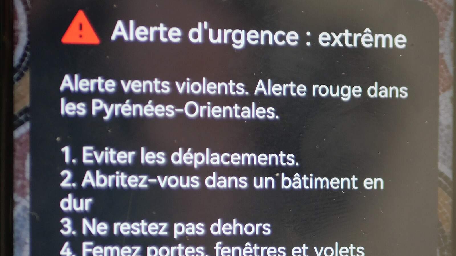 Écran de smartphone affichant une notification FR-Alert « Alerte d'urgence : extrême » reçue pendant une tempête, avec les consignes des autorités