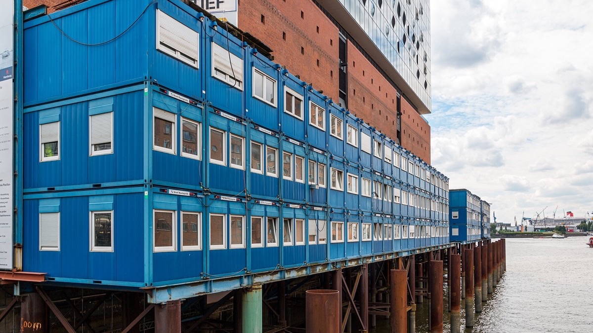 Maison moderne faite de conteneurs maritimes empilés, avec bardage et grandes baies vitrées, dans un jardin verdoyant