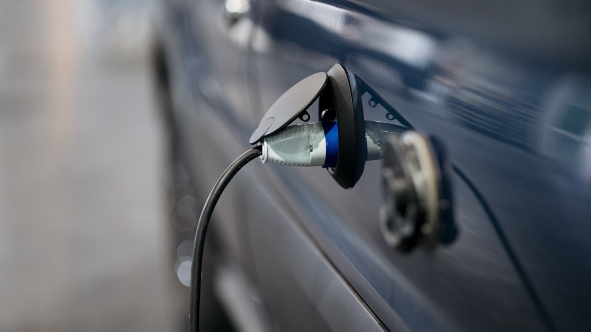 Une berline hybride rechargeable branchée sur une prise de recharge domestique, capot ouvert évoquant l'entretien mécanique